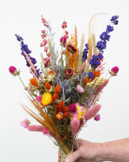 Luxe droogbloemen boeket met statice, craspedia en warme tinten in studiolicht vastgehouden in de hand.